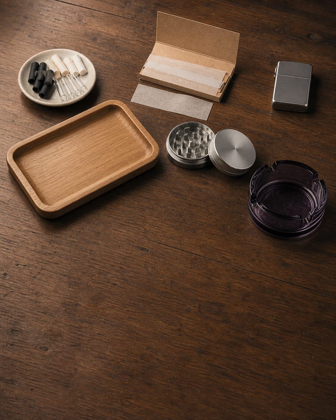 Bandeja de madera, grinder abierto, papel de liar, filtros, encendedor metálico y cenicero sobre una mesa de madera. Bandeja de madera, grinder abierto, papel de liar, filtros, encendedor metálico y cenicero sobre una mesa de madera.