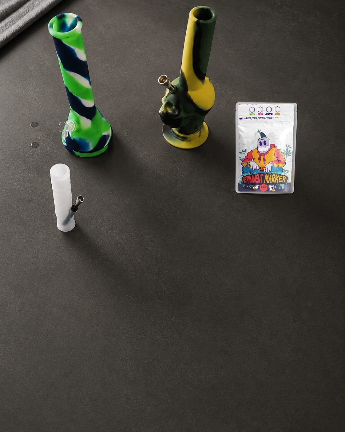 Tres bongs sobre una superficie oscura: uno alto verde, azul y blanco, otro amarillo y verde con rostro y uno blanco pequeño. Tres bongs sobre una superficie oscura: uno alto verde, azul y blanco, otro amarillo y verde con rostro y uno blanco pequeño.