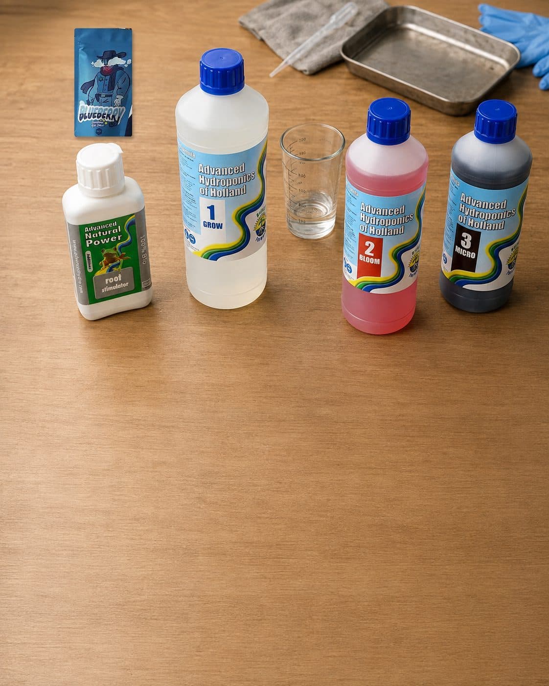 Botellas de Advanced Hydroponics Grow, Bloom, Micro y estimulador de raíces junto a un vaso medidor sobre una mesa. Botellas de Advanced Hydroponics Grow, Bloom, Micro y estimulador de raíces junto a un vaso medidor sobre una mesa.