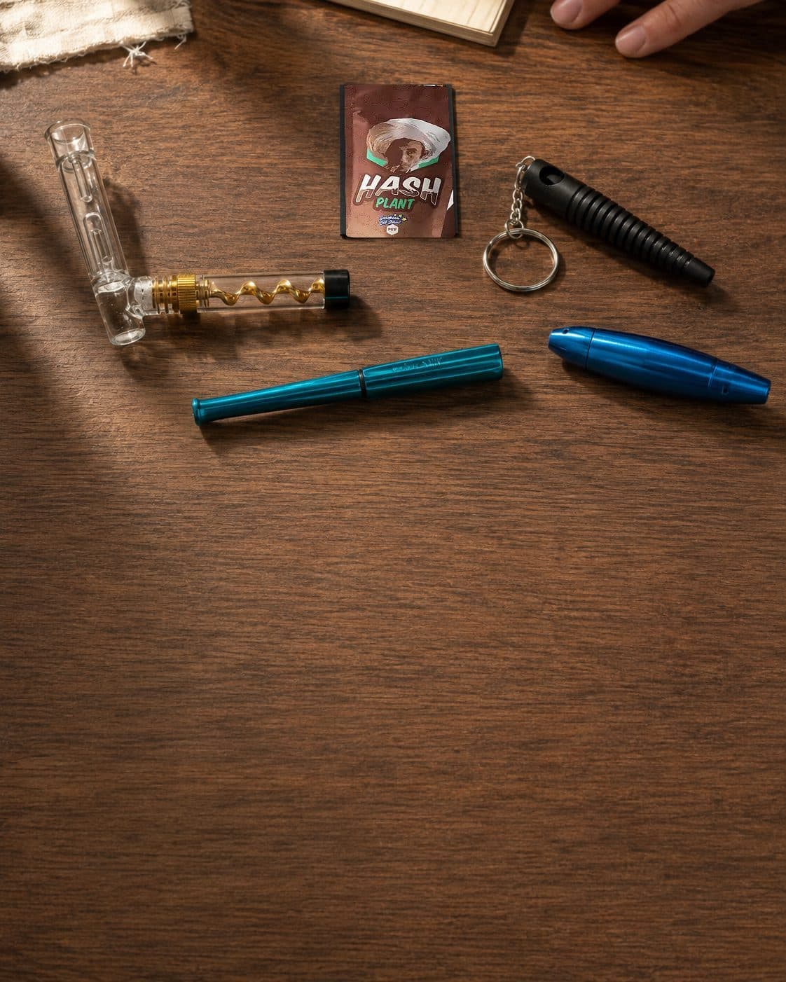 Selección de pipas de distintas formas, dos azules y una negra con llavero, junto a una pieza transparente sobre una mesa de madera. Selección de pipas de distintas formas, dos azules y una negra con llavero, junto a una pieza transparente sobre una mesa de madera.