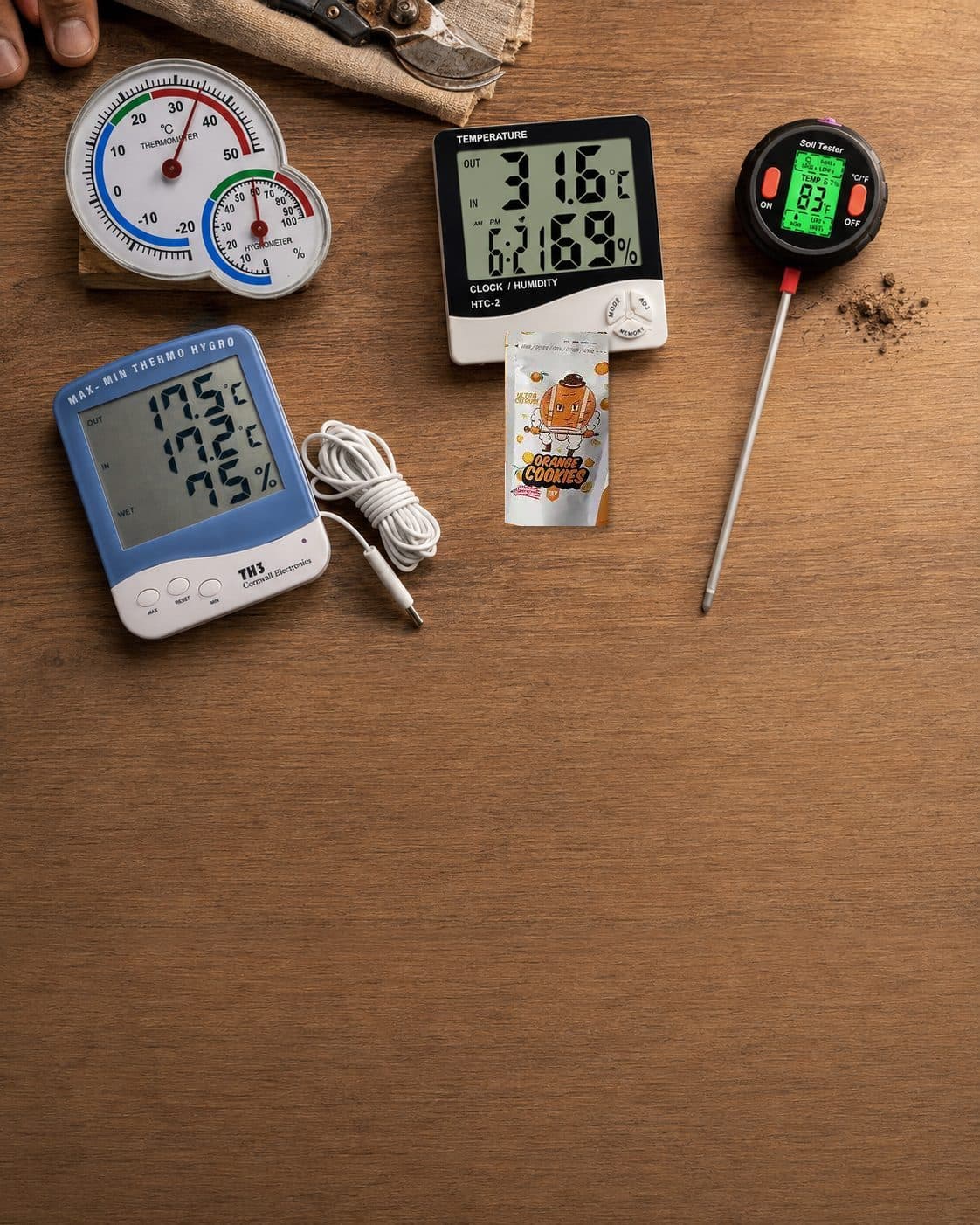 Termohigrómetros analógicos y digitales, medidor con sonda y sobre de Orange Cookies sobre una mesa de madera. Termohigrómetros analógicos y digitales, medidor con sonda y sobre de Orange Cookies sobre una mesa de madera.