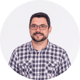 Retrato circular de un hombre con pelo corto oscuro, gafas, barba y camisa de cuadros sobre fondo claro.