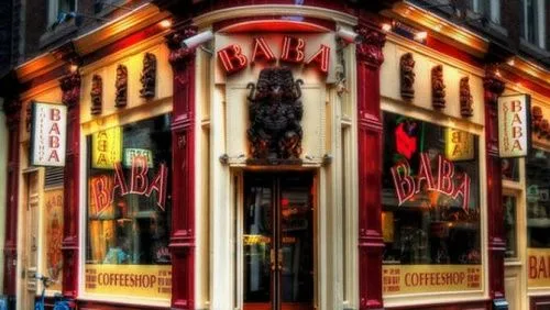 Fachada del coffeeshop Baba en una esquina, con marcos rojos, grandes escaparates, rótulos «BABA» y una figura sobre la entrada. Fachada del coffeeshop Baba en una esquina, con marcos rojos, grandes escaparates, rótulos «BABA» y una figura sobre la entrada.