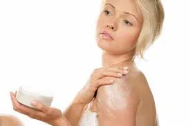 Mujer aplicándose crema blanca en el hombro con una mano mientras sostiene un pequeño recipiente con la otra. Mujer aplicándose crema blanca en el hombro con una mano mientras sostiene un pequeño recipiente con la otra.