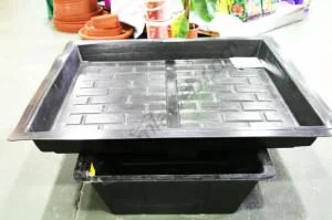 Bandeja rectangular negra con canales en el fondo, colocada sobre un depósito en una zona de cultivo. Bandeja rectangular negra con canales en el fondo, colocada sobre un depósito en una zona de cultivo.