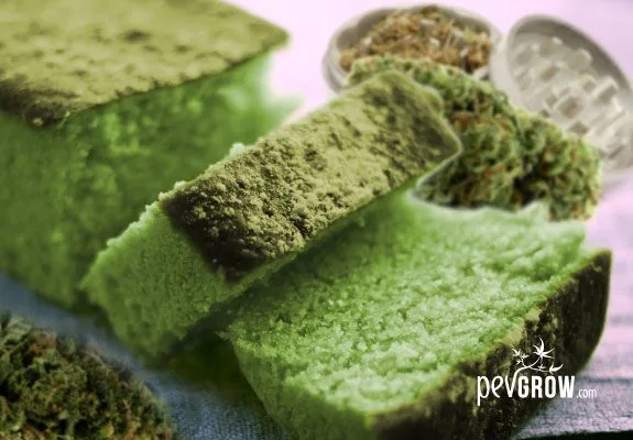 Bizcocho verde cortado en rebanadas, con cogollos de cannabis y un grinder abierto al fondo.