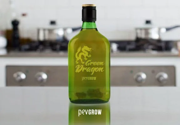 Botella verde con tapón negro y rótulo «Green Dragon», sobre una encimera reflectante con fogones desenfocados al fondo. Botella verde con tapón negro y rótulo «Green Dragon», sobre una encimera reflectante con fogones desenfocados al fondo.