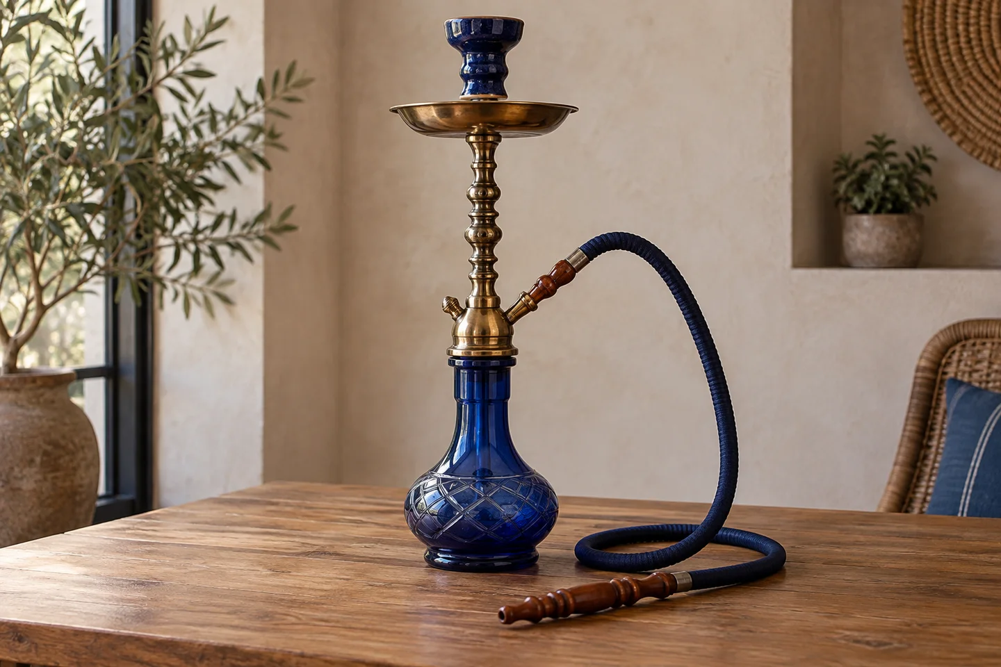 Cachimba con base de vidrio azul, cuerpo dorado y manguera azul con boquilla de madera sobre una mesa. Cachimba con base de vidrio azul, cuerpo dorado y manguera azul con boquilla de madera sobre una mesa.
