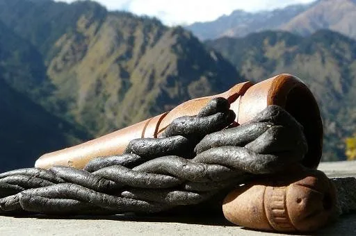 Barras oscuras de charas entrelazadas junto a un chilum marrón, sobre una superficie de piedra con montañas al fondo.