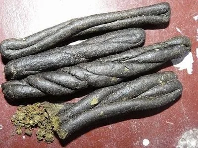 Varias barras oscuras de charas, algunas retorcidas y trenzadas, sobre una superficie rojiza con pequeños fragmentos sueltos.