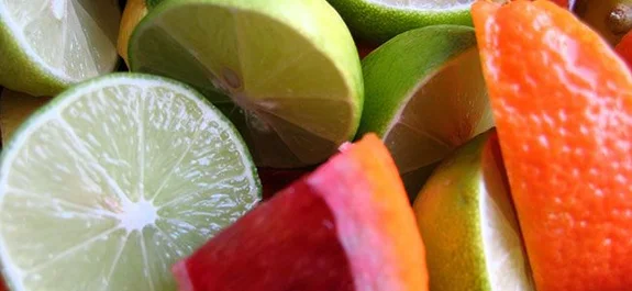 Primer plano de cítricos cortados, con rodajas de lima de pulpa verde clara y gajos de tonos rosados y anaranjados.