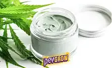 Tarro abierto con crema de tono claro y marcas en la superficie, junto a su tapa y hojas de cannabis sobre fondo blanco.