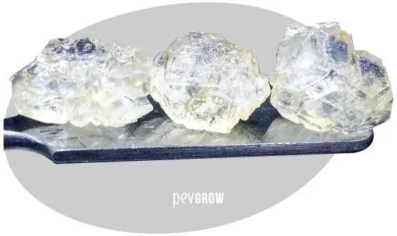 Tres masas cristalinas translúcidas e irregulares sobre una pala metálica plana, con fondo gris y marca Pevgrow.