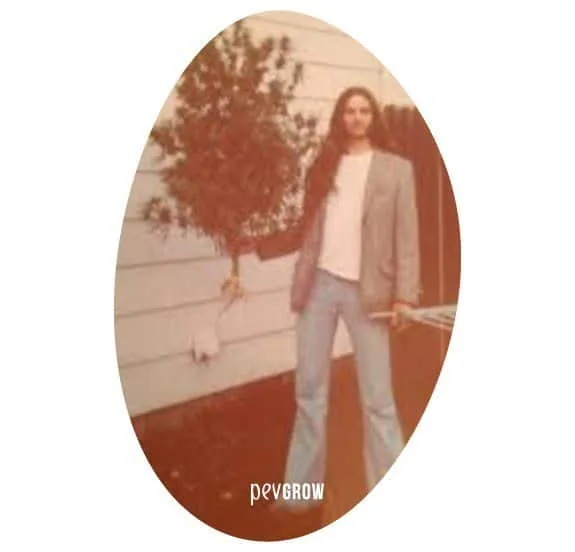 Fotografía antigua en recorte ovalado de una persona de pelo largo junto a una planta alta, frente a una pared exterior. Fotografía antigua en recorte ovalado de una persona de pelo largo junto a una planta alta, frente a una pared exterior.