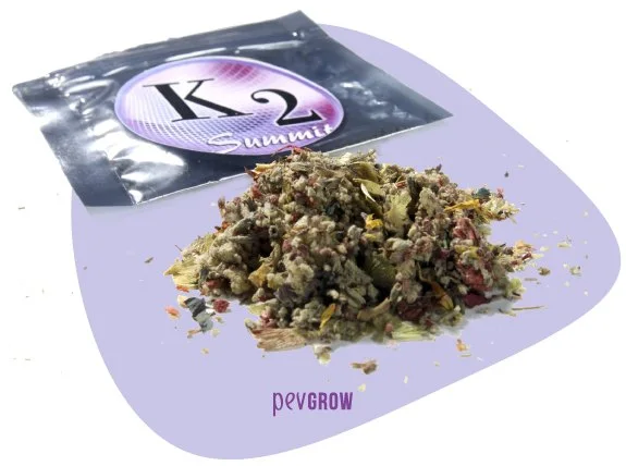 Montón de fragmentos vegetales secos junto a una bolsa plateada con la etiqueta «K2 Summit», sobre un fondo lila. Montón de fragmentos vegetales secos junto a una bolsa plateada con la etiqueta «K2 Summit», sobre un fondo lila.