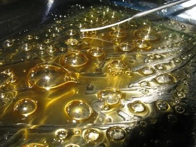 Primer plano de un extracto de color ámbar con numerosas burbujas de distintos tamaños y una varilla metálica en la parte superior. Primer plano de un extracto de color ámbar con numerosas burbujas de distintos tamaños y una varilla metálica en la parte superior.