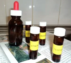 Frasco oscuro con cuentagotas rojo junto a cuatro frascos pequeños con tapas blancas y etiquetas amarillas, sobre papeles.