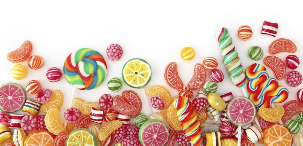 Caramelos multicolores, piruletas en espiral y golosinas con formas de cítricos sobre fondo blanco. Caramelos multicolores, piruletas en espiral y golosinas con formas de cítricos sobre fondo blanco.
