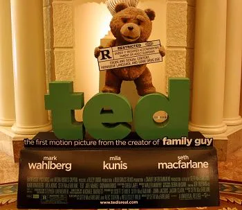 Expositor promocional de Ted con un oso de peluche que sostiene un cartel de clasificación R sobre grandes letras verdes.