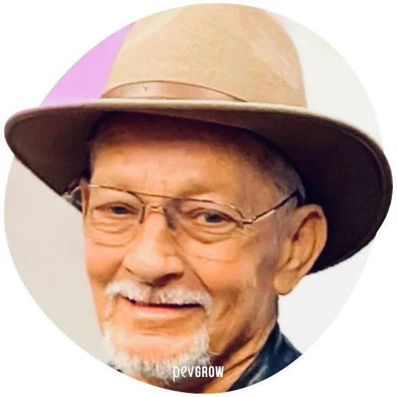 Retrato circular de un hombre sonriente con gafas, sombrero de ala ancha, bigote blanco y perilla, con la marca Pevgrow al pie. Retrato circular de un hombre sonriente con gafas, sombrero de ala ancha, bigote blanco y perilla, con la marca Pevgrow al pie.