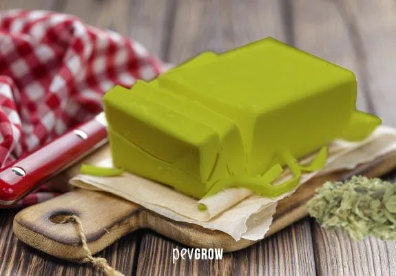 Bloque de mantequilla verde con virutas sobre papel y una tabla de madera, junto a cogollos y un paño de cuadros. Bloque de mantequilla verde con virutas sobre papel y una tabla de madera, junto a cogollos y un paño de cuadros.