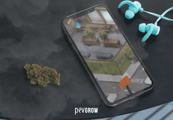 Móvil en diagonal con un videojuego en pantalla, auriculares turquesa y un cogollo sobre una superficie oscura.