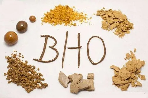 Muestras doradas y marrones en bolas, polvo, grumos y fragmentos alrededor de las letras BHO, trazadas sobre un fondo claro.