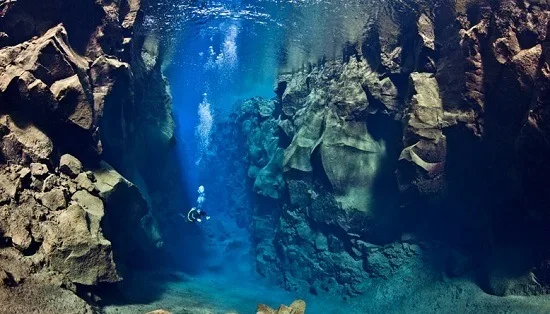 Buceador entre paredes de roca en una grieta submarina de agua azul, con luz que entra desde la superficie. Buceador entre paredes de roca en una grieta submarina de agua azul, con luz que entra desde la superficie.