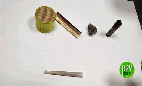 Porro sobre una superficie blanca, con un grinder verde, papel de liar, un cogollo y un mechero dispuestos en la parte superior.