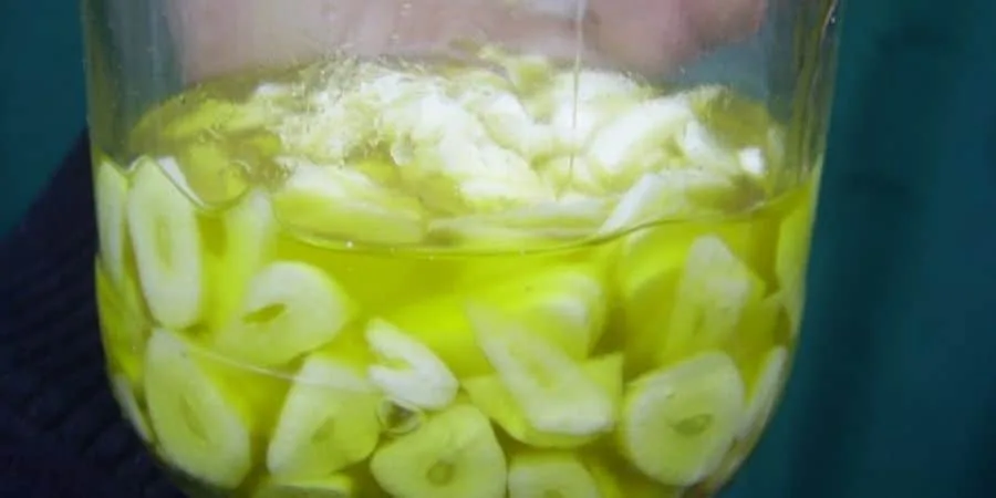 Primer plano de un recipiente transparente con trozos de ajo sumergidos en un líquido amarillo verdoso.