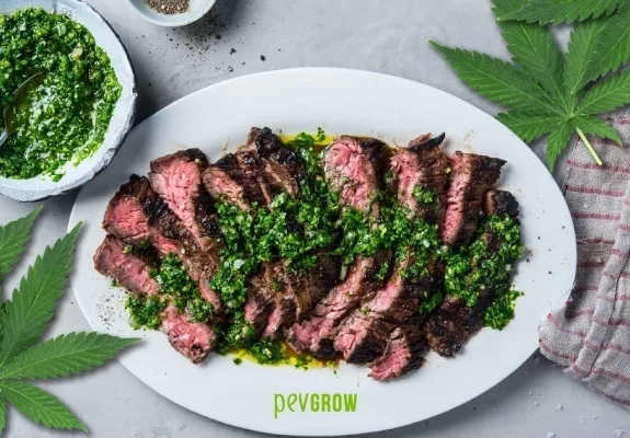 Chuletón cortado en tiras, con el centro rosado y salsa chimichurri verde, en un plato blanco rodeado de hojas de cannabis. Chuletón cortado en tiras, con el centro rosado y salsa chimichurri verde, en un plato blanco rodeado de hojas de cannabis.