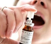 Primer plano de una persona con la boca abierta que sostiene un frasco con pulverizador blanco dirigido hacia el interior. Primer plano de una persona con la boca abierta que sostiene un frasco con pulverizador blanco dirigido hacia el interior.