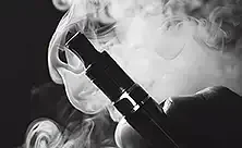 Dispositivo de vapeo sostenido entre dedos en una fotografía en blanco y negro con una nube
