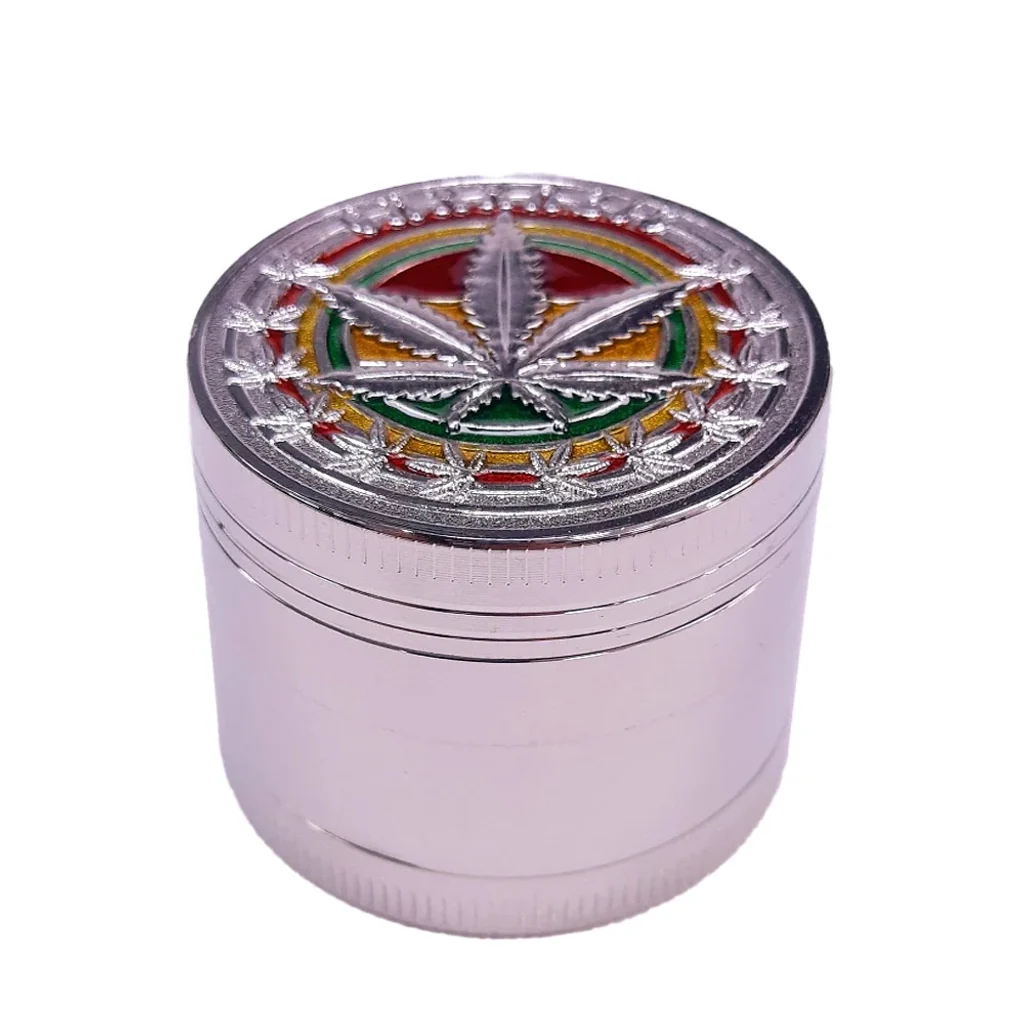 Grinder cilíndrico plateado con tapa decorada con una hoja de cannabis en relieve sobre franjas rojas, amarillas y verdes.