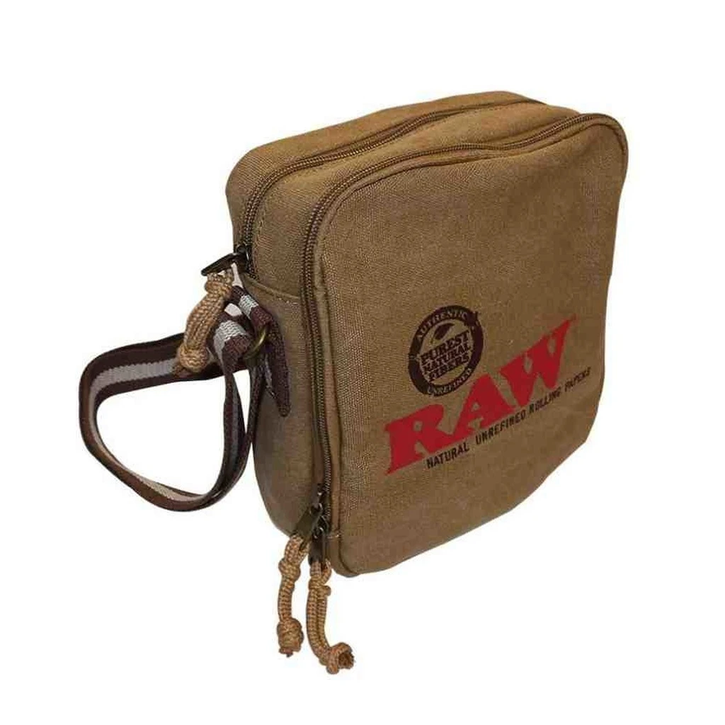 Bandolera RAW marrón vista en ángulo, con logotipo rojo, compartimentos con cremallera, tiradores de cordón y correa lateral.