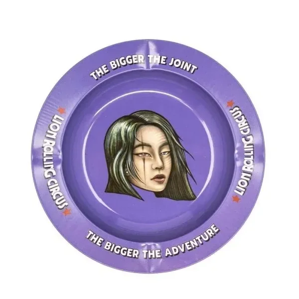Cenicero Rolling Circus Tora Tora circular y morado, con un rostro femenino ilustrado en el centro y lemas blancos en el borde.