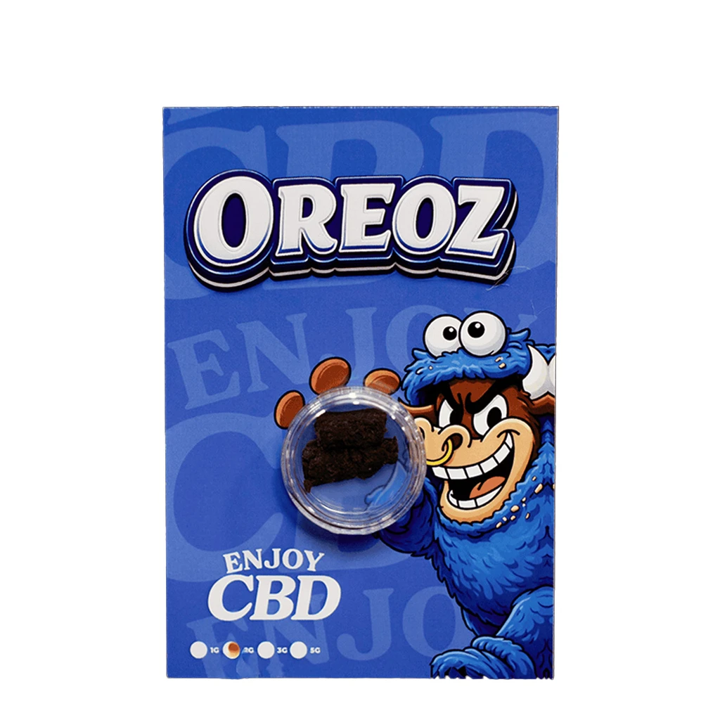 Envase azul de Enjoy CBD Oreoz con un personaje de dibujos y un recipiente transparente que muestra fragmentos oscuros de hachís.