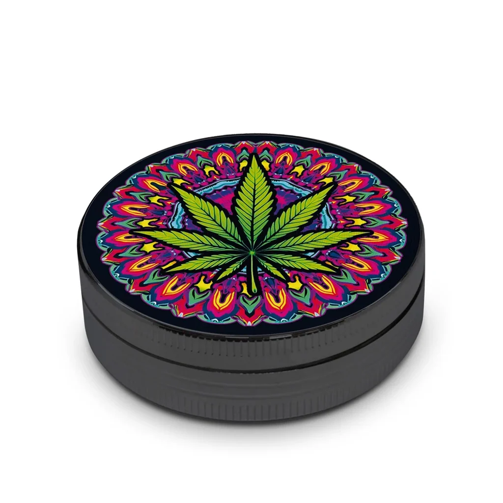 Grinder negro cerrado, visto en perspectiva, con una hoja de cannabis verde sobre un motivo psicodélico multicolor en la tapa.
