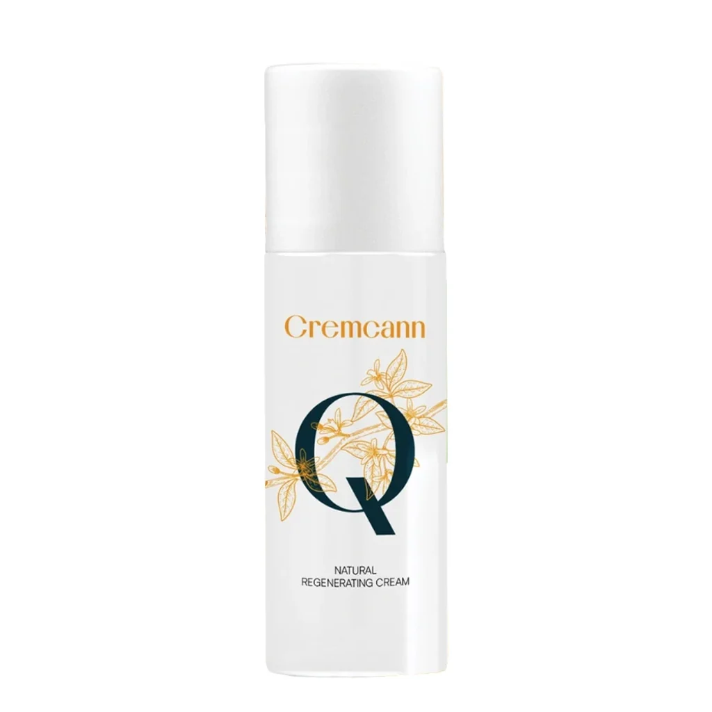 Envase blanco de crema Cremcann, con tapón alto, motivos botánicos dorados y una gran Q oscura sobre fondo blanco.
