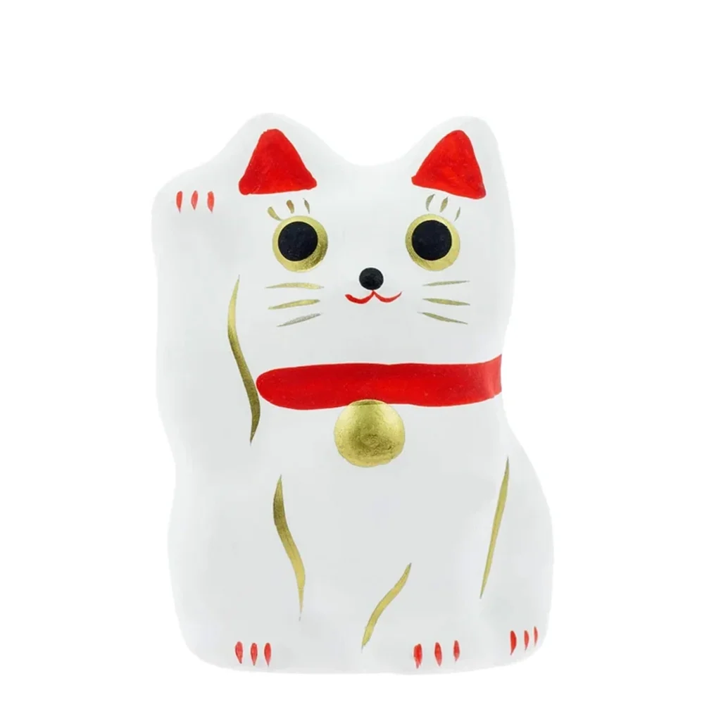 Figura Maneki Neko blanca con una pata levantada, orejas y collar rojos, cascabel dorado y grandes ojos negros. Figura Maneki Neko blanca con una pata levantada, orejas y collar rojos, cascabel dorado y grandes ojos negros.