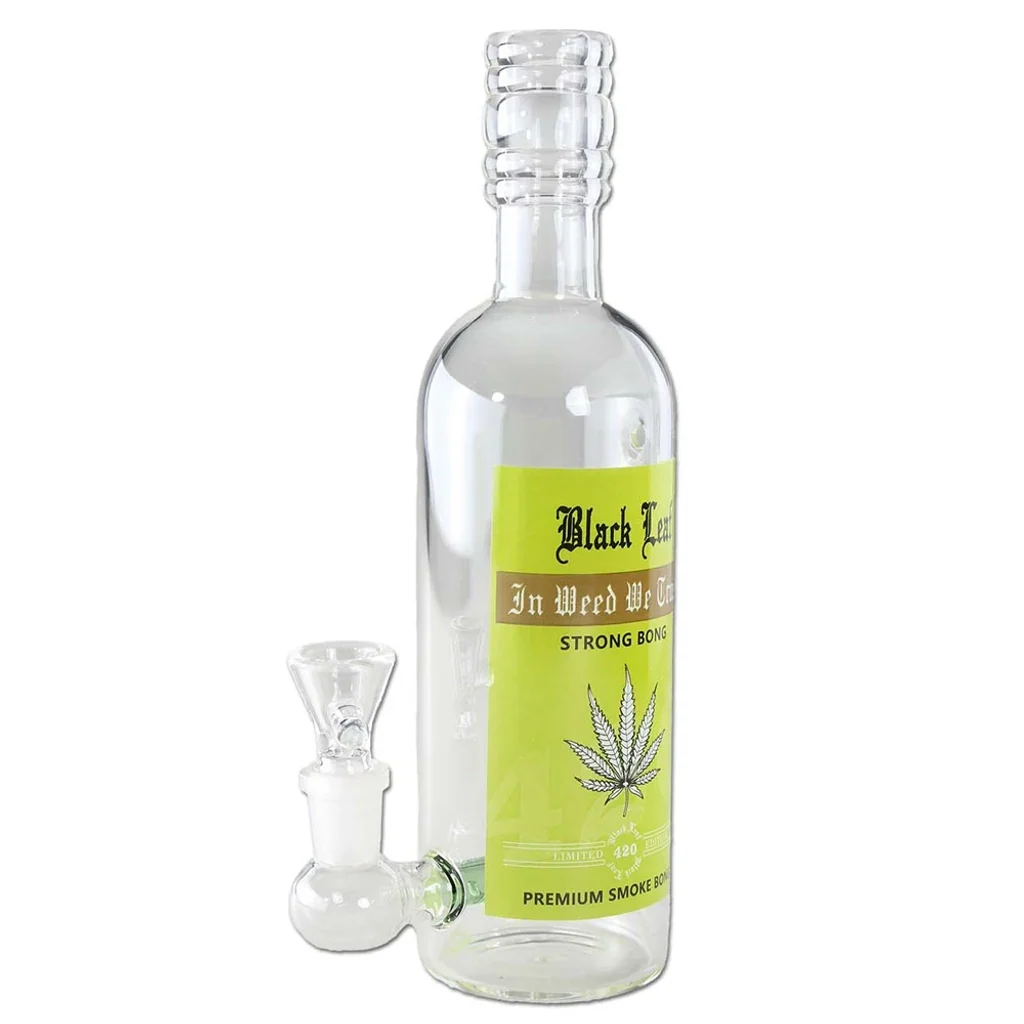 Bong transparente con forma de botella de licor, cuello con relieves, cazoleta lateral y etiqueta verde con una hoja de cannabis.