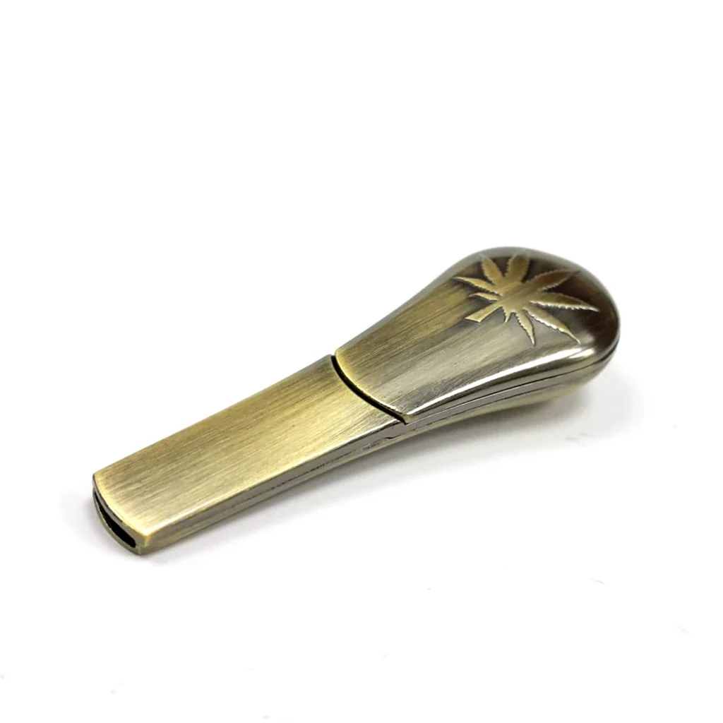 Pipa Gold Leaf de tono dorado envejecido, alargada y con extremo redondeado decorado con una hoja de cannabis, sobre fondo blanco.