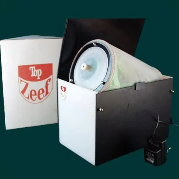 Polinizador Top Zeef abierto, con tambor cilíndrico de malla en su interior, caja de marca al lado y accesorio conectado por cable. Polinizador Top Zeef abierto, con tambor cilíndrico de malla en su interior, caja de marca al lado y accesorio conectado por cable.