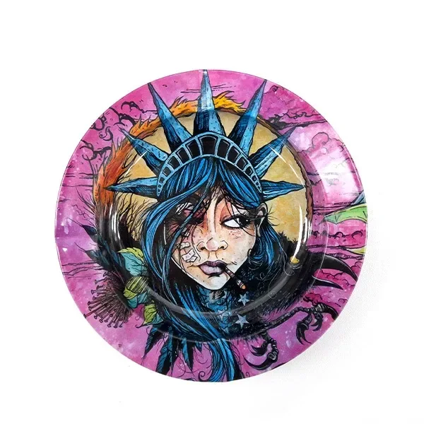 Cenicero redondo Basic Liberty con ilustración de una mujer de pelo azul y corona de puntas sobre un fondo rosa y amarillo.