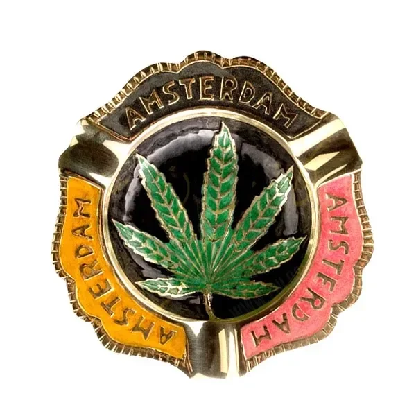 Cenicero de acabado dorado con hoja de cannabis verde en el centro, tres apoyos y la palabra Amsterdam sobre zonas negras, amarillas y rojas.