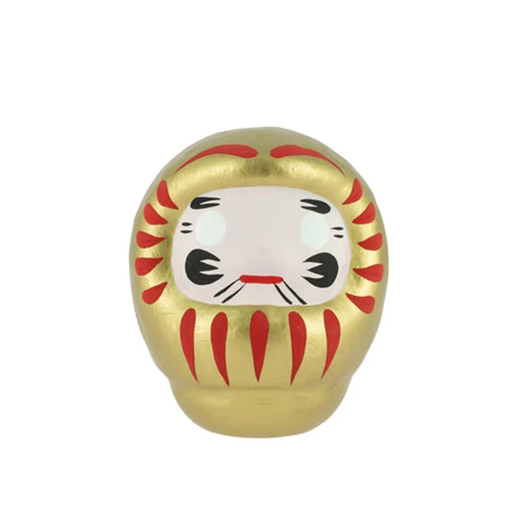 Daruma dorado de cuerpo redondeado con trazos rojos, rostro blanco y detalles negros, presentado de frente sobre fondo blanco. Daruma dorado de cuerpo redondeado con trazos rojos, rostro blanco y detalles negros, presentado de frente sobre fondo blanco.
