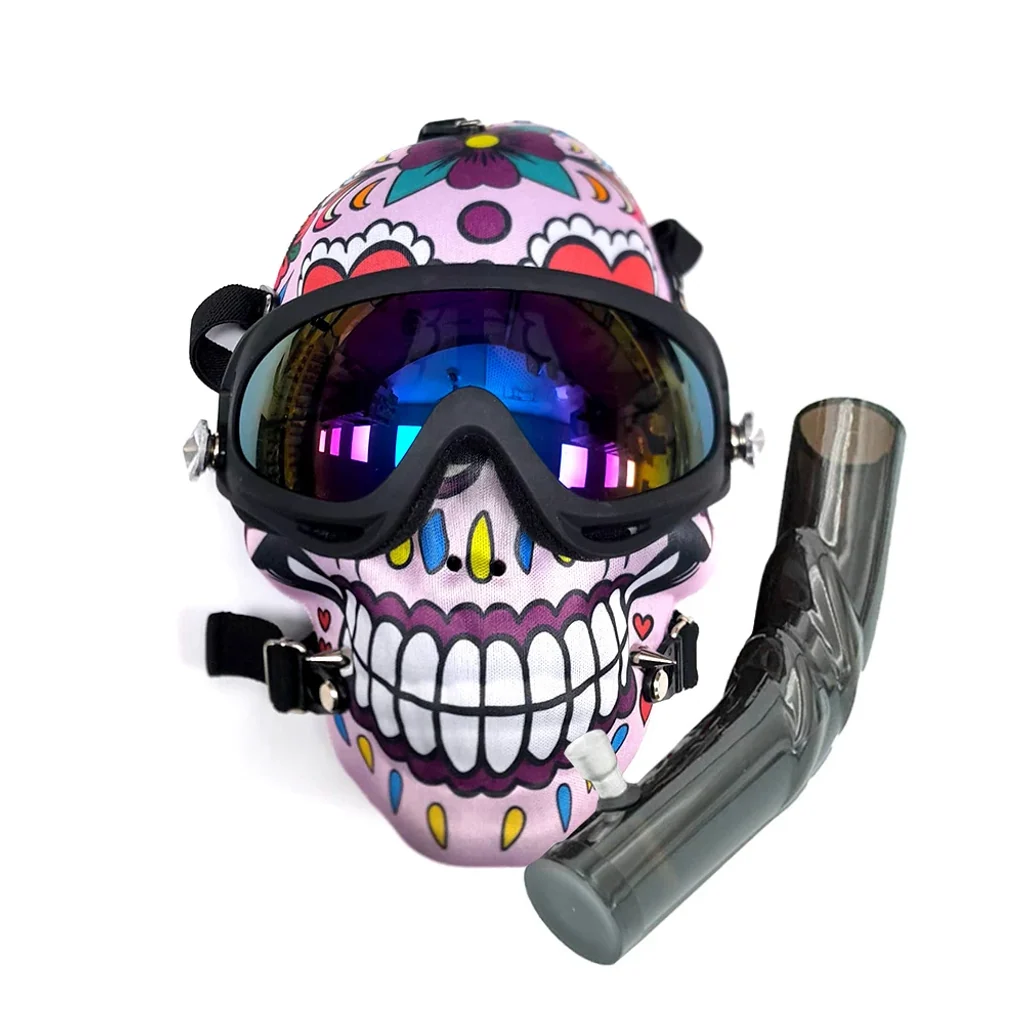 Máscara con calavera multicolor, gafas oscuras de reflejos violetas y azules y correas negras, junto a un tubo curvo ahumado con cazoleta.
