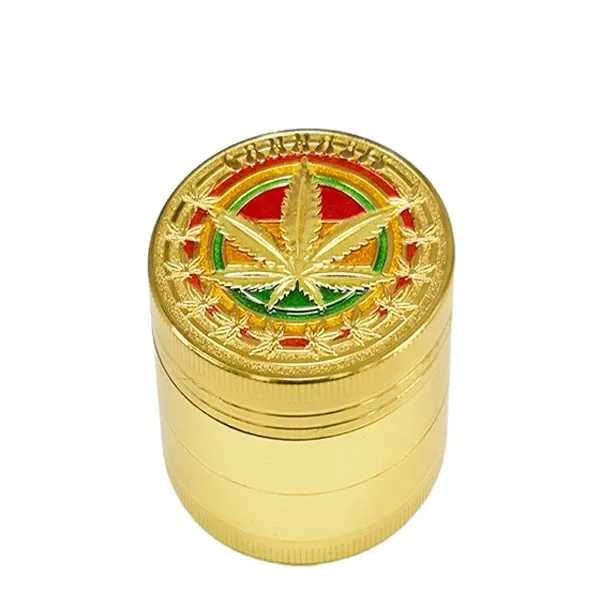 Grinder cilíndrico dorado visto en perspectiva, con una hoja de cannabis en relieve sobre un motivo rojo, amarillo y verde.