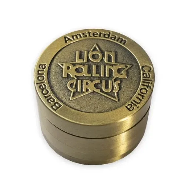 Grinder Rolling Circus de color dorado, visto en perspectiva, con logotipo en relieve y nombres de ciudades alrededor de la tapa.