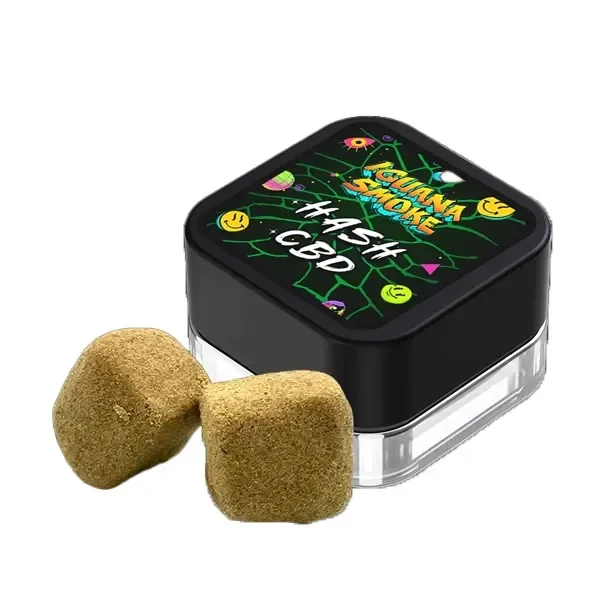 Dos bloques dorados de Hash CBD Iguana Smoke Blonde junto a un recipiente cuadrado con tapa negra y etiqueta de colores.